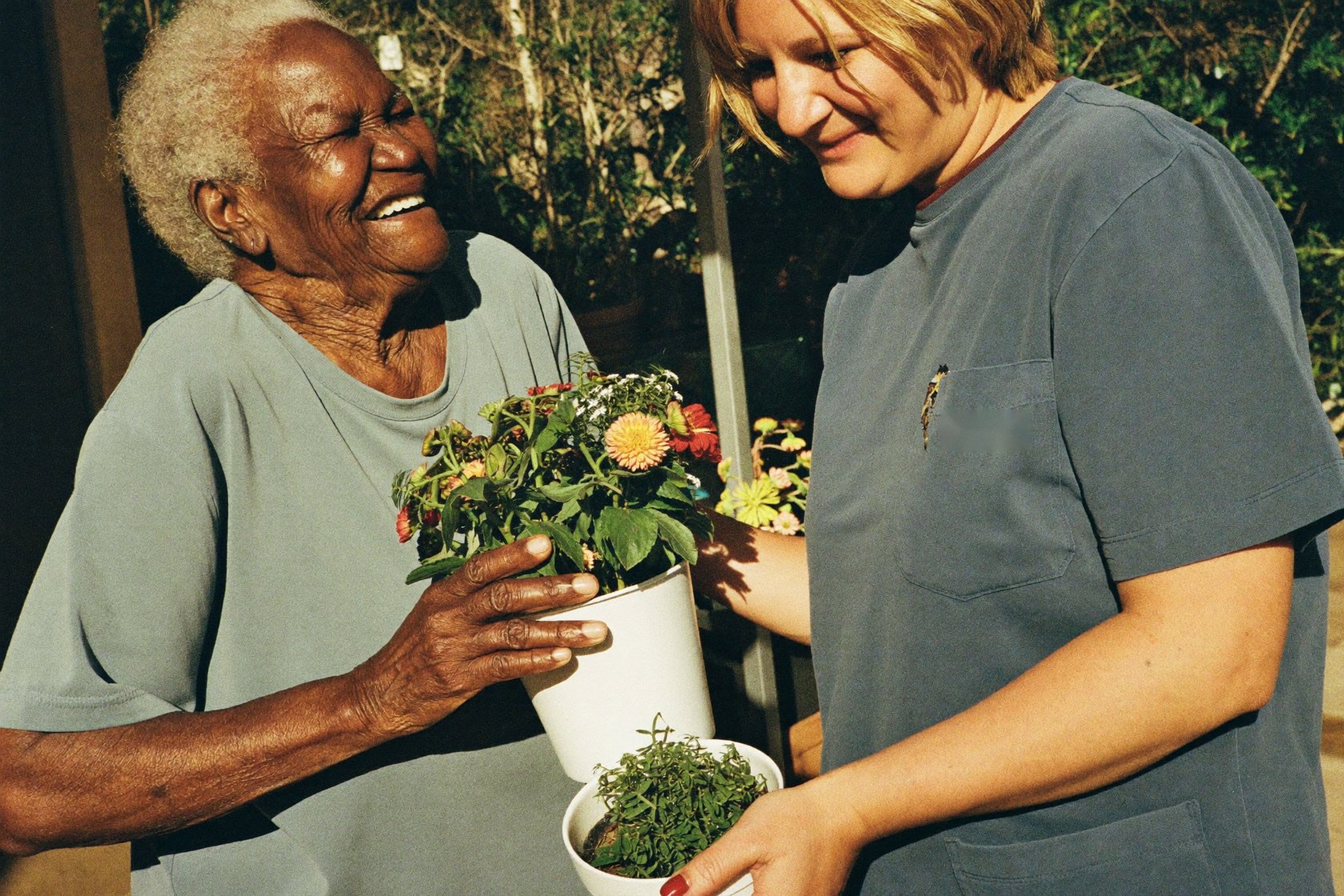 A senior woman and her caregiver tending potted plants together on a sunny patio