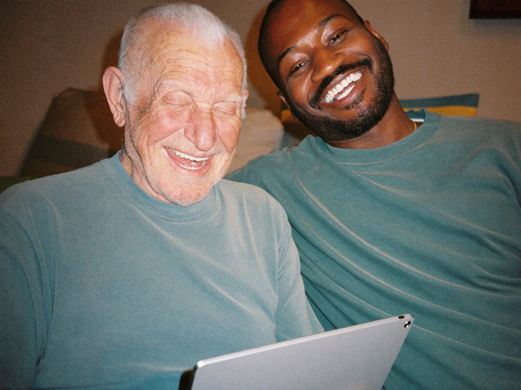 A senior man and his caregiver looking at a tablet together on the sofa