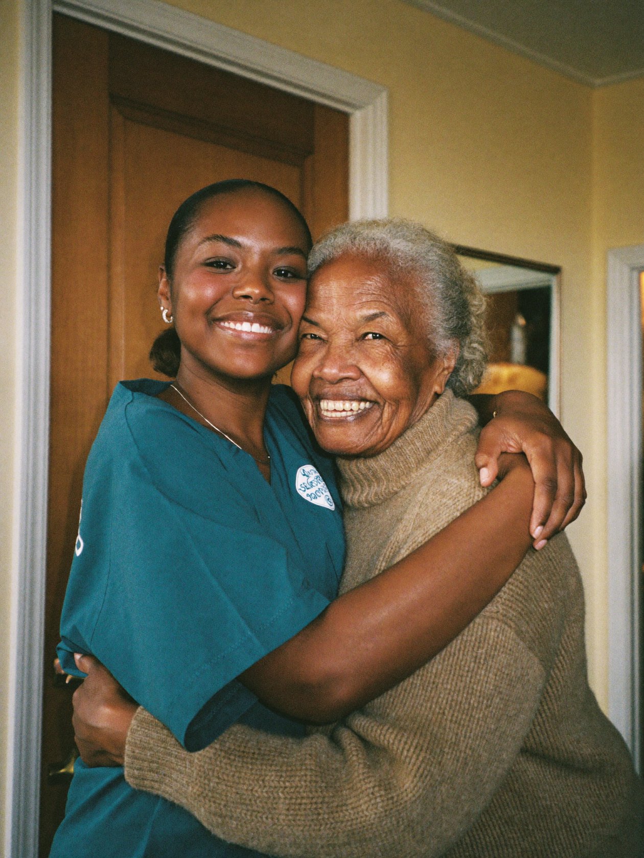An adult daughter embracing her senior mother at the front door