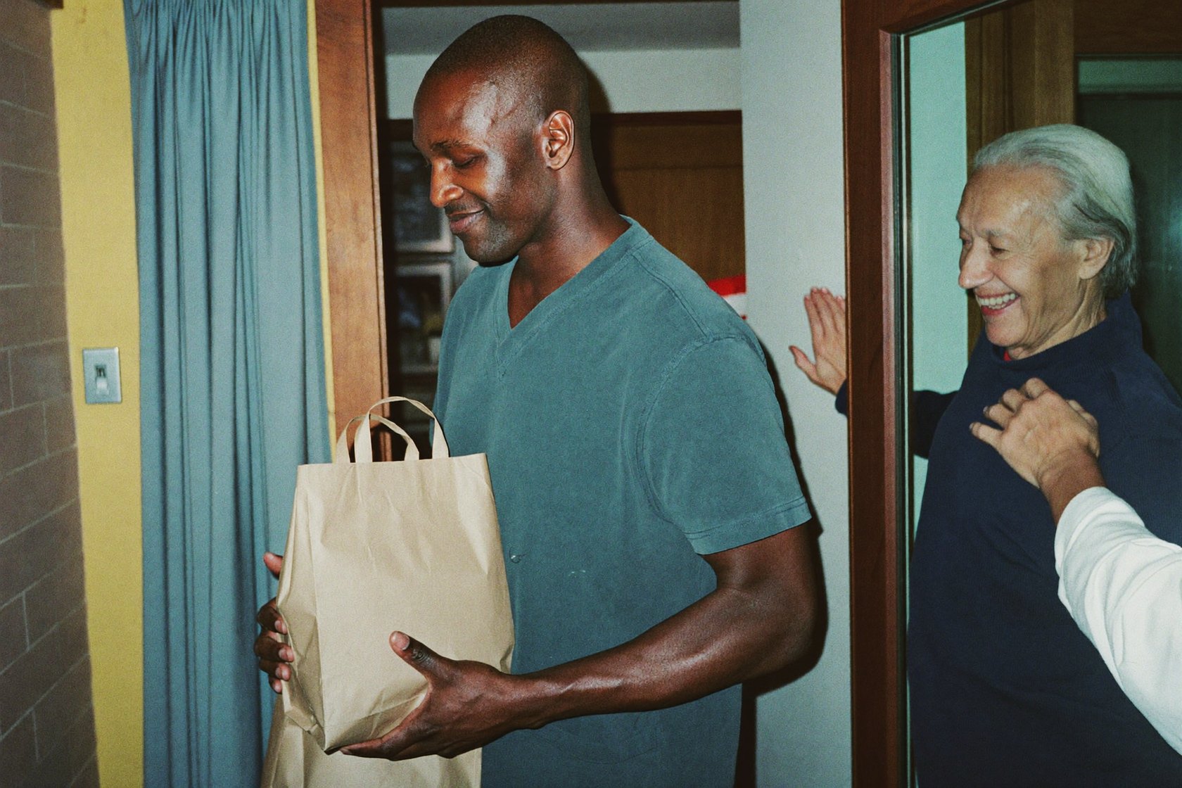 A caregiver carrying grocery bags into a senior man's home