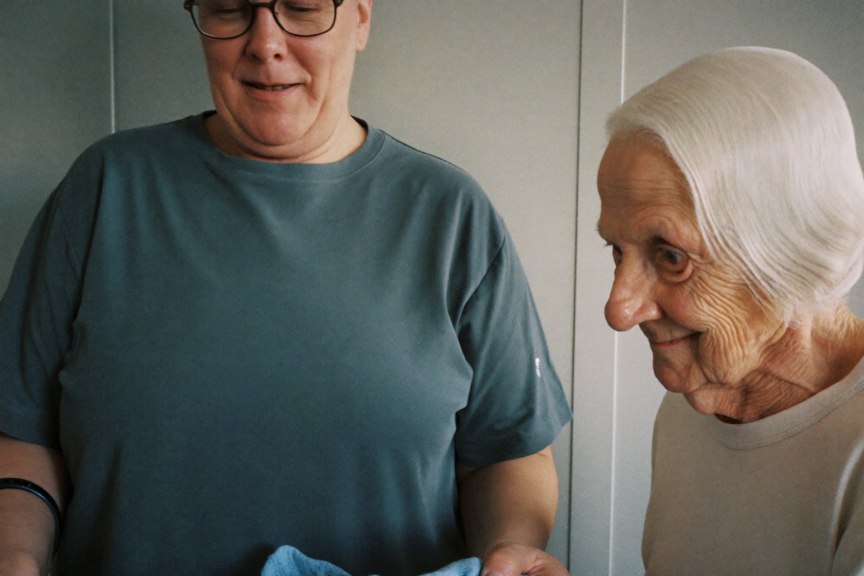 A caregiver folding fresh laundry while chatting with a senior woman