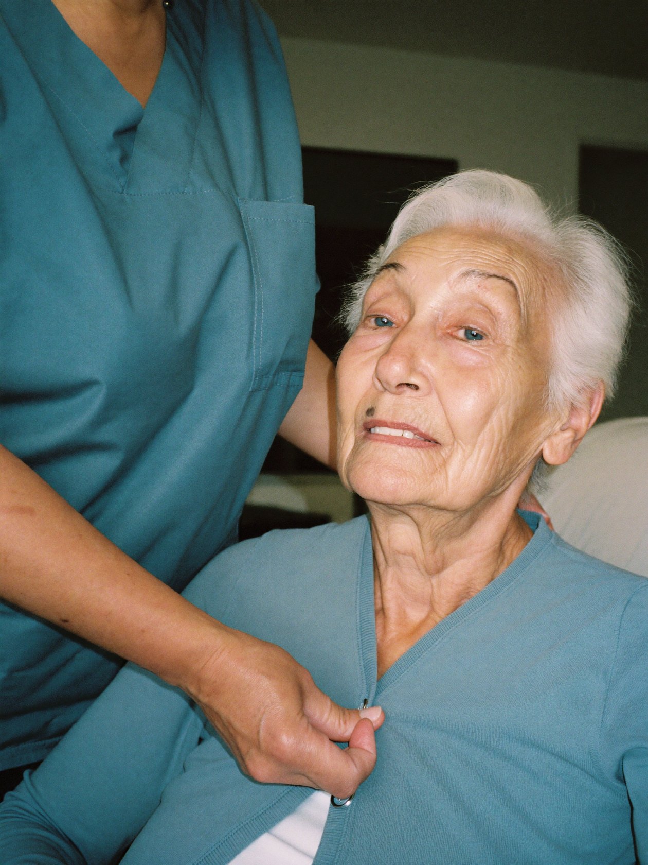 A caregiver helping a senior woman button her cardigan