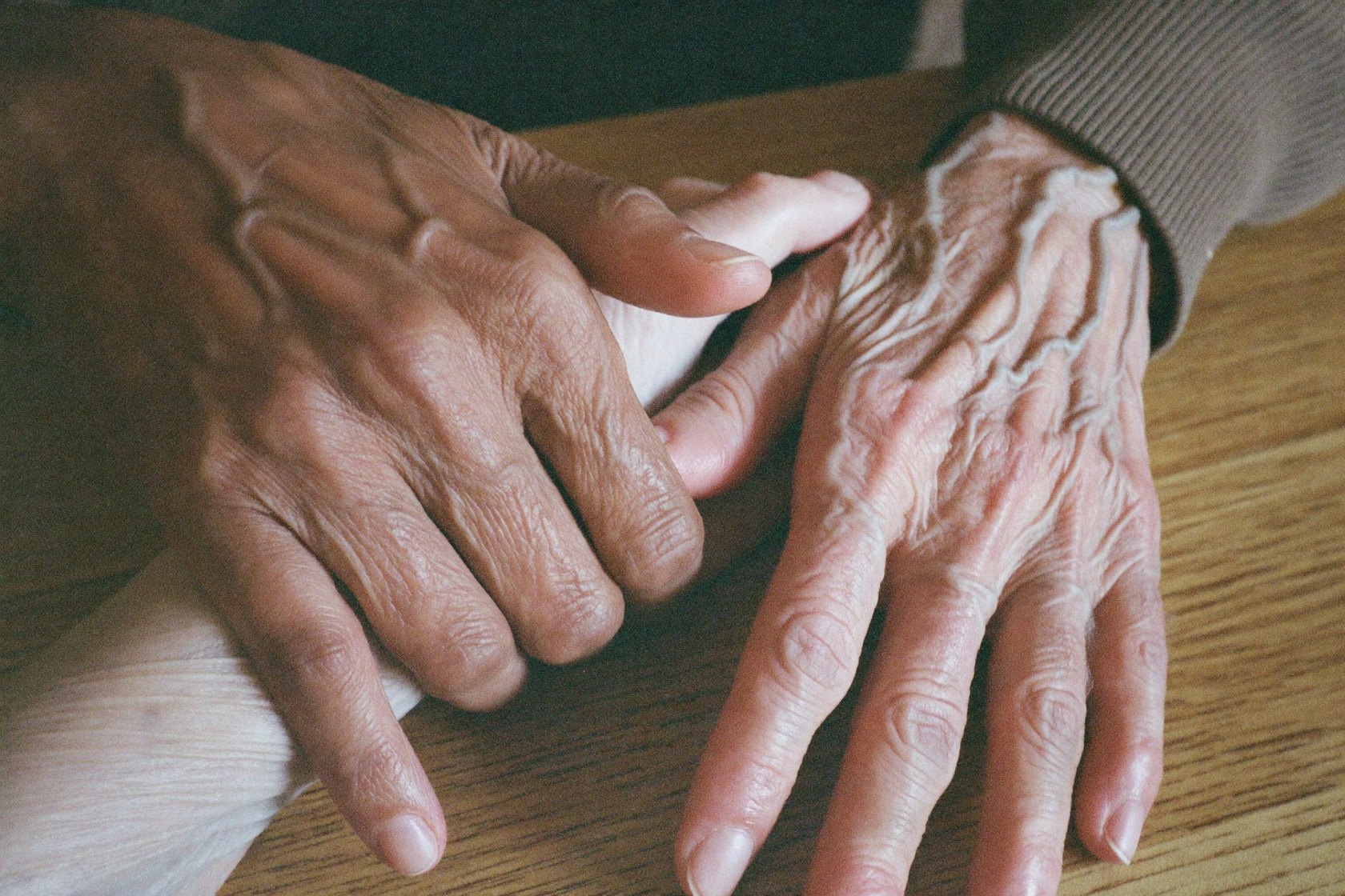 A caregiver's hands gently holding a senior's hands